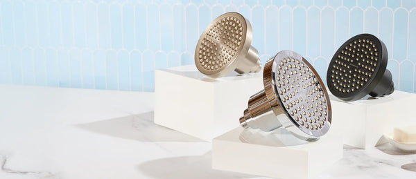 Three Filtered Showerheads on separate pedestals. One is chrome, one is black, and the last is brushed nickel. They're in front of a soft blue tiled background.