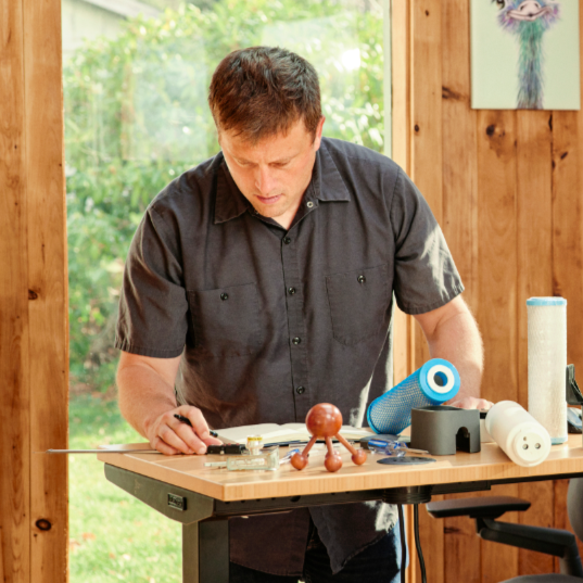 Dr. Eric Roy working on a Hydroviv refill cartridge with papers and scientific models on the desk before him.