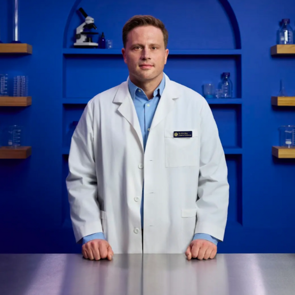 Dr. Eric Roy in a lab coat standing in a laboratory setting with shelves and equipment.
