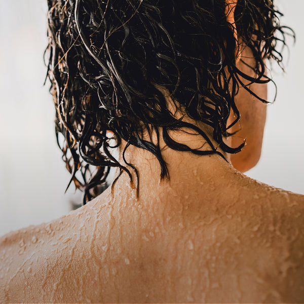 A photo of an individual's back, shoulders and up, as they shower.