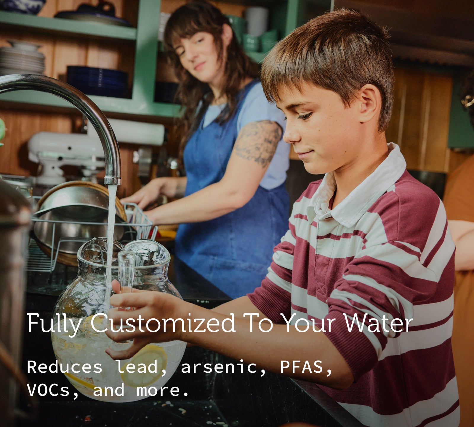 A photo of a boy filling up a pitcher of water at the kitchen faucet as his mom looks on.
