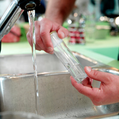 person taking tap water sample from kitchen faucet